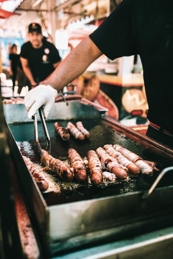 Close-up view of a street vendor grilling sausages outdoors, showcasing vibrant street food culture.