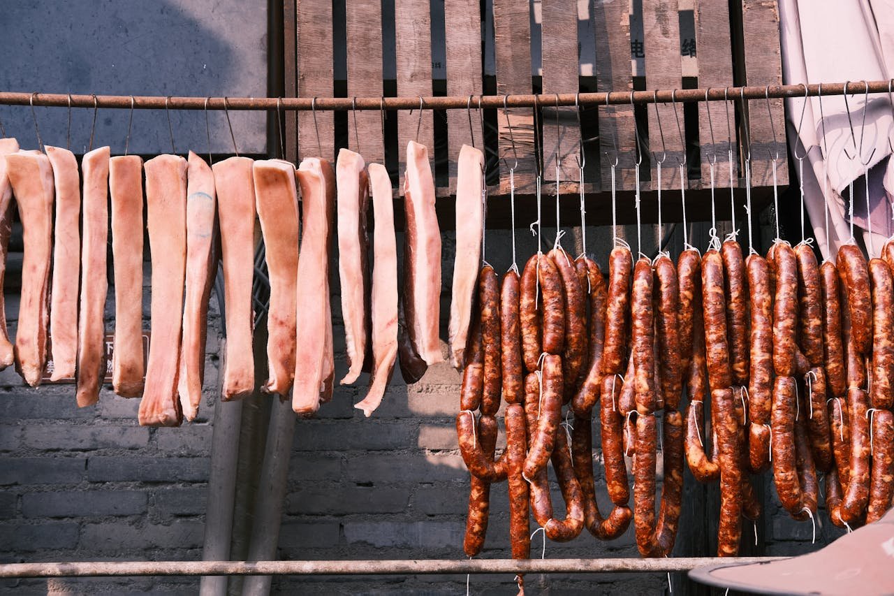 Embutidos Huétor Tájar Granada. Raw meat strips and sausages drying outdoors, showcasing traditional food preservation methods.