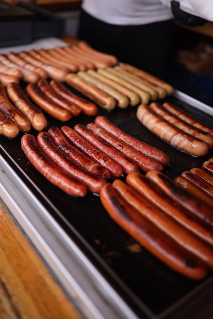 Venta Embutidos en Granada . Close-up of various types of grilled sausages on a hot tray, perfect for BBQ or food stalls.